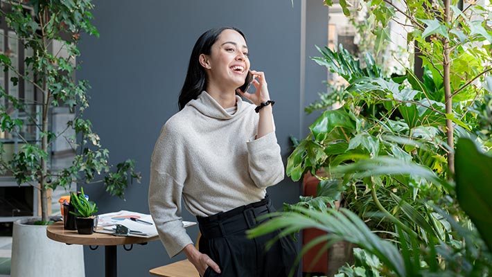 A woman standing near the garden area and smiling while talking on phone