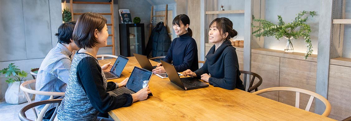 Four professional women laughing and discussing while working with a laptop