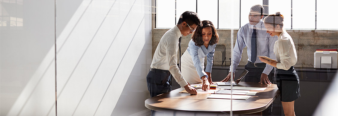 Four business colleagues stand talking in a meeting room