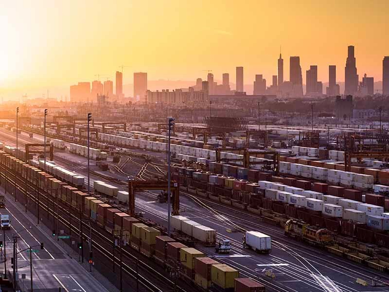 City view with cargo containers on a railway track, being loaded and unloaded
