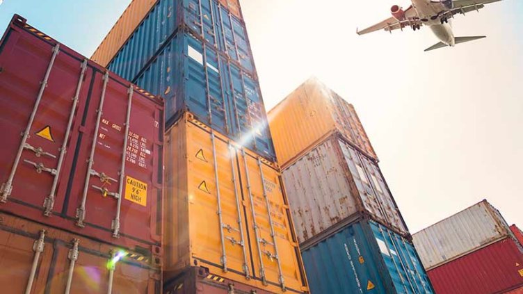 A plane flying over a stack of shipping containers