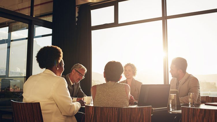 Diverse group of businesspeople sitting together around a table in a boardroom during a late afternoon office meeting
