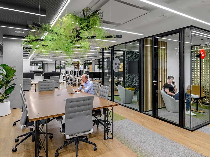 One person sitting at his desk and another person inside a glass cubicle