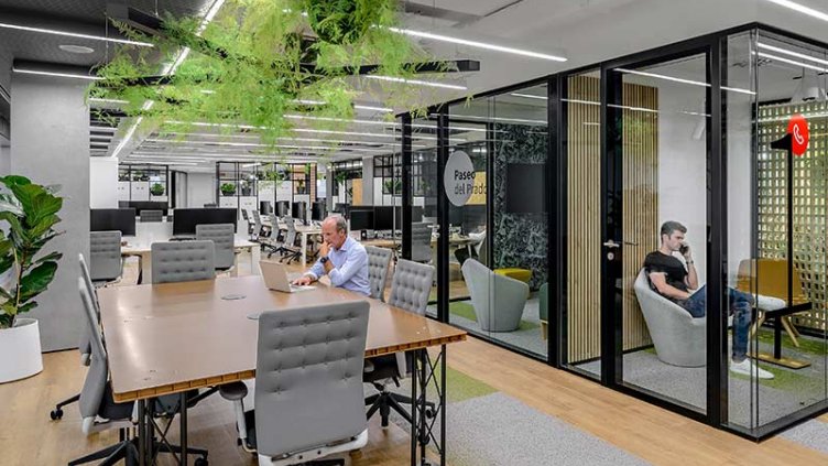 One person sitting at his desk and another person inside a glass cubicle